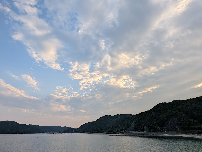 水辺を囲む山と、淡い金色の光が広がる雲
