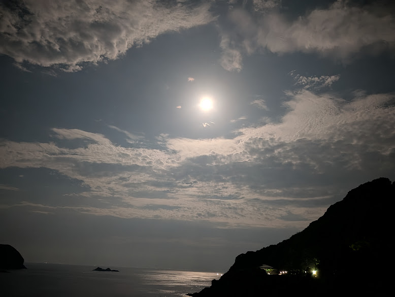 雲に囲まれた明るい月と、月明かりが映る夜の海